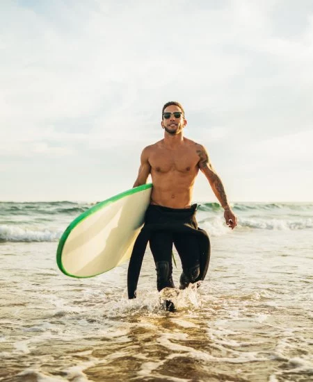 A,man,wearing,a,wetsuit,and,sunglasses,walks,out,of